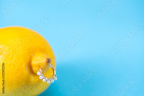 Intimate piercing. Minimal piercing concept. Lemon with piercing on blue background