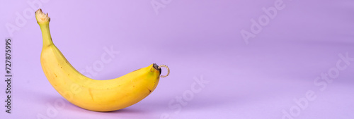 Intimate piercing. Minimal piercing concept. Banana with piercing on a lilac background