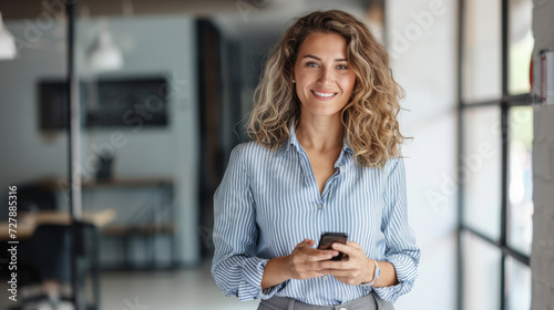 Smiling woman holding a smartphone in a modern office setting. © MP Studio