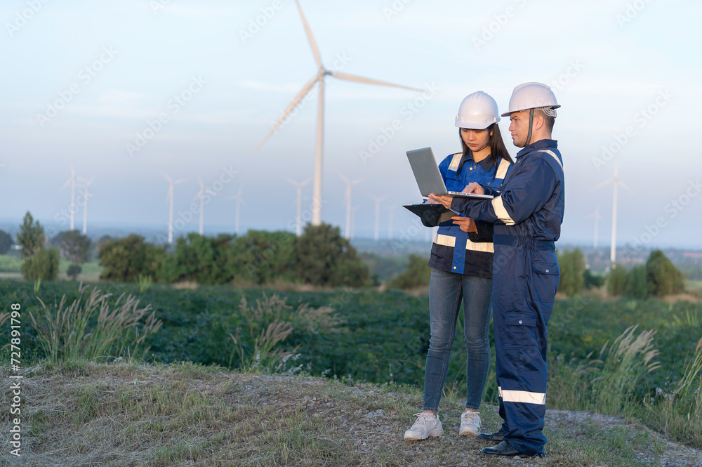 Two engineers working and holding the report at wind turbine farm Power Generator Station on mountain,Thailand people,Technician man and woman discuss about work Two engineers working and holding the report at wind turbine farm Power Generator Station on mountain,Thailand people,Technician man and woman discuss about work