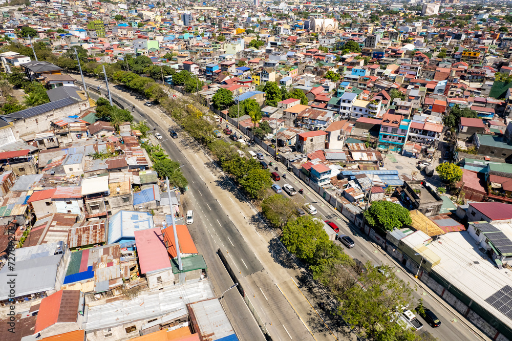 Taguig, Metro Manila, Philippines - Feb 03, 2024: Aerial view of C5 road cutting through a dense urban area with colorful houses and traffic
