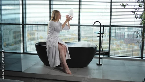 Spa relaxation. Young woman in spa bathrobe sitting at bath with foam in bathtub. Girl relaxing in bathroom at home. Female spending morning in bathroom. Beauty treatment body skin care concept photo