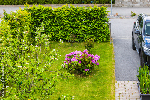 Beautiful view of a garden with blooming flowers and a car parked on the parking lot of a private villa during a warm spring day. Sweden.
