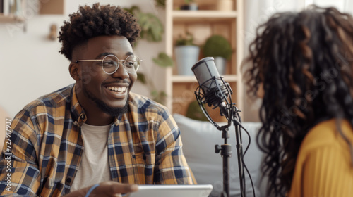 young person with glasses is smiling at a person holding a tablet, with a microphone in the foreground, suggesting an interview or podcast setting. © MP Studio