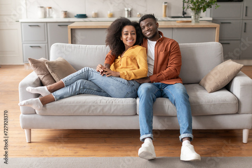 Happy Black Couple Chilling On Sofa In Modern Living Room