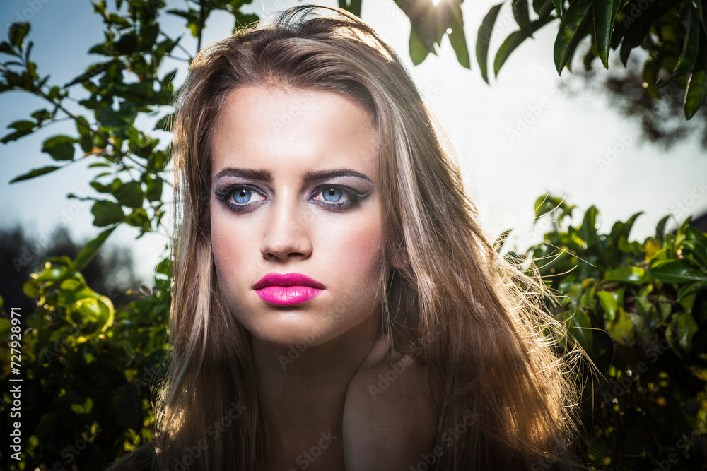 Young blond woman standing by hedge outdoors Young blond woman standing by hedge outdoors