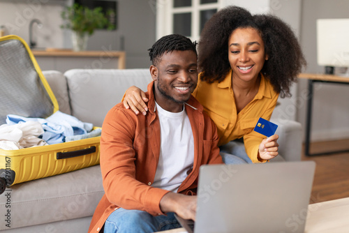 african couple using laptop and credit card booking tour indoor photo
