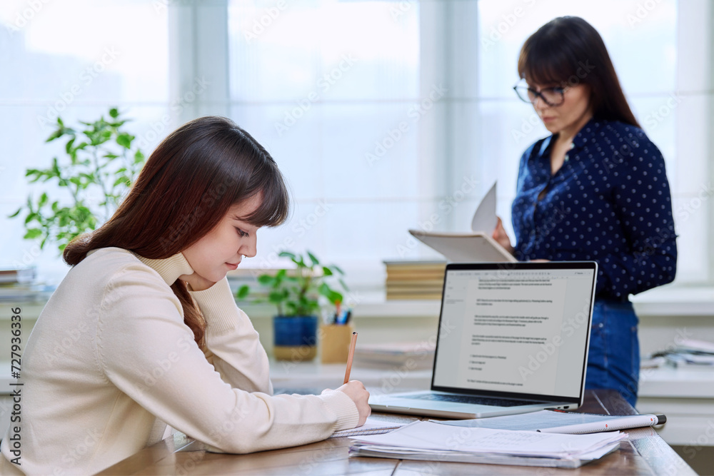 Teenage student studying at desk with computer, trainer mentor helping teaching Teenage student studying at desk with computer, trainer mentor helping teaching