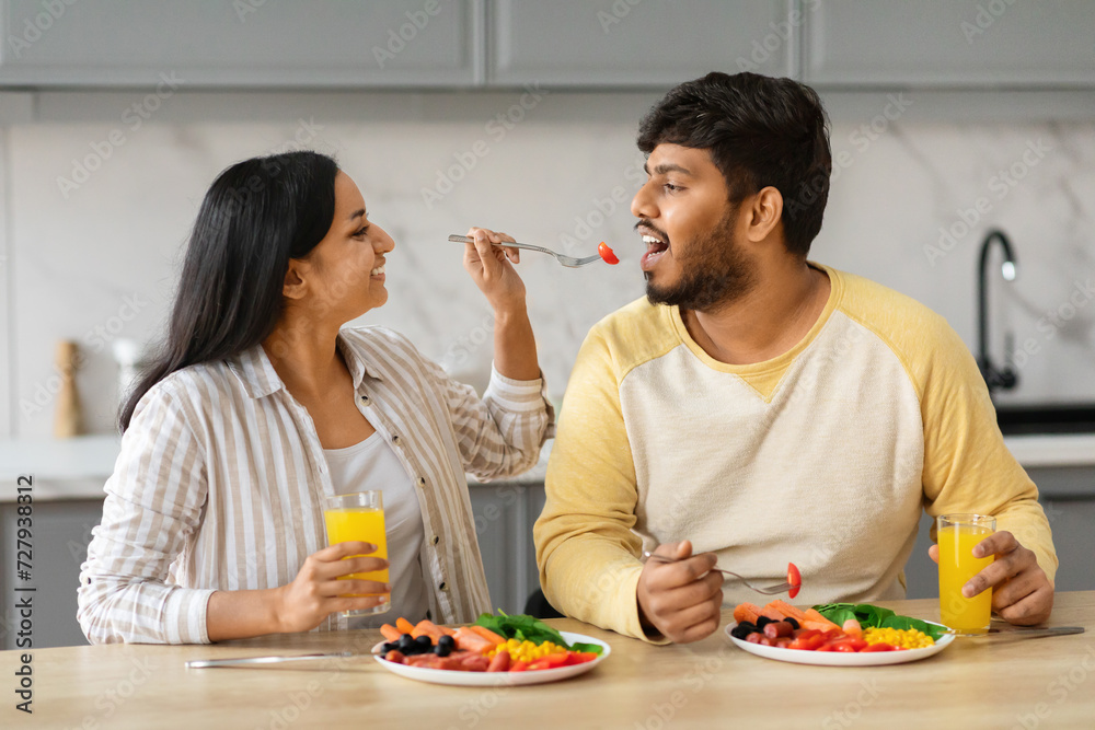 Pretty young indian woman feeding her husband, kitchen interior Pretty young indian woman feeding her husband, kitchen interior