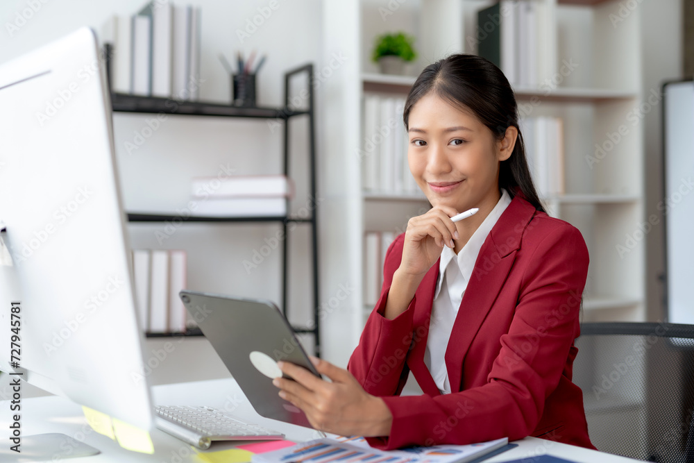 Professional young Asian businesswoman smiling while working on a digital tablet in a modern office setting. Professional young Asian businesswoman smiling while working on a digital tablet in a modern office setting.