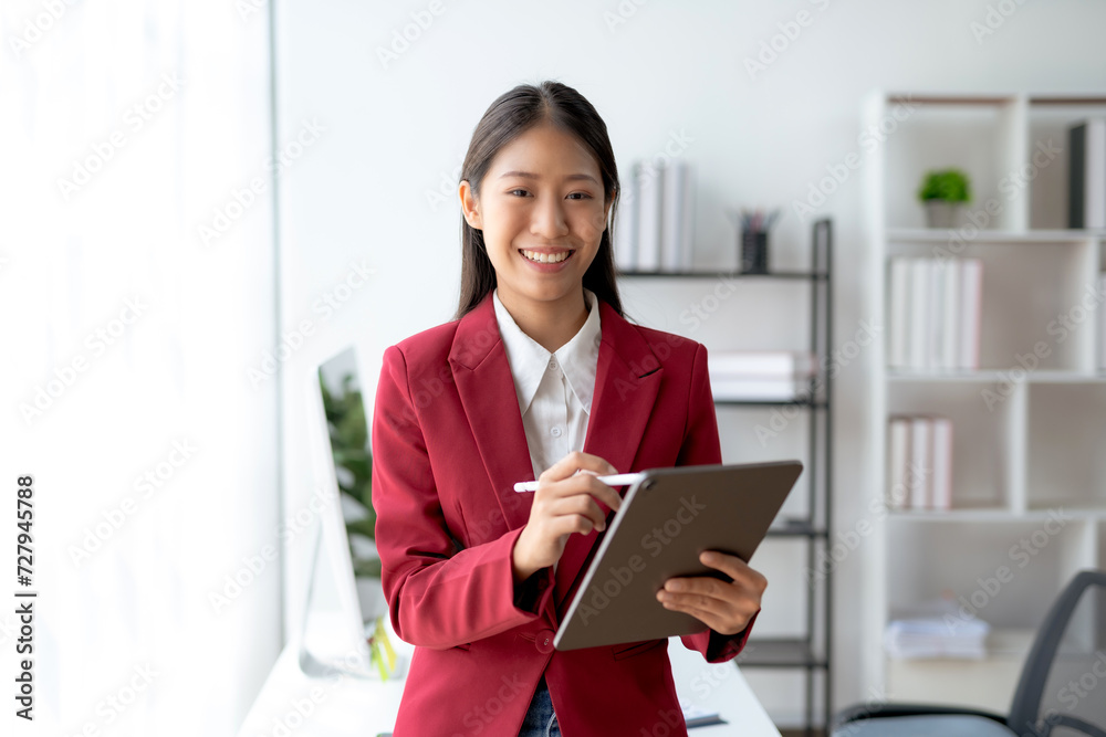 Professional young Asian businesswoman smiling while working on a digital tablet in a modern office setting. Professional young Asian businesswoman smiling while working on a digital tablet in a modern office setting.