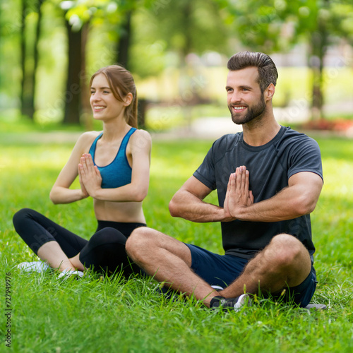 Full body young couple sitting in lotus position or woman practicing with man, male bearded coach trainer, doing yoga exercises or meditating together, after outside training. Square image.