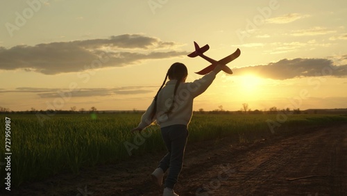 Kid aviator dreams of flying and becoming pilot. Little girl child wants to become pilot and astronaut. Slow motion. Happy girl runs with toy airplane on field in sunset light. Child play toy airplane