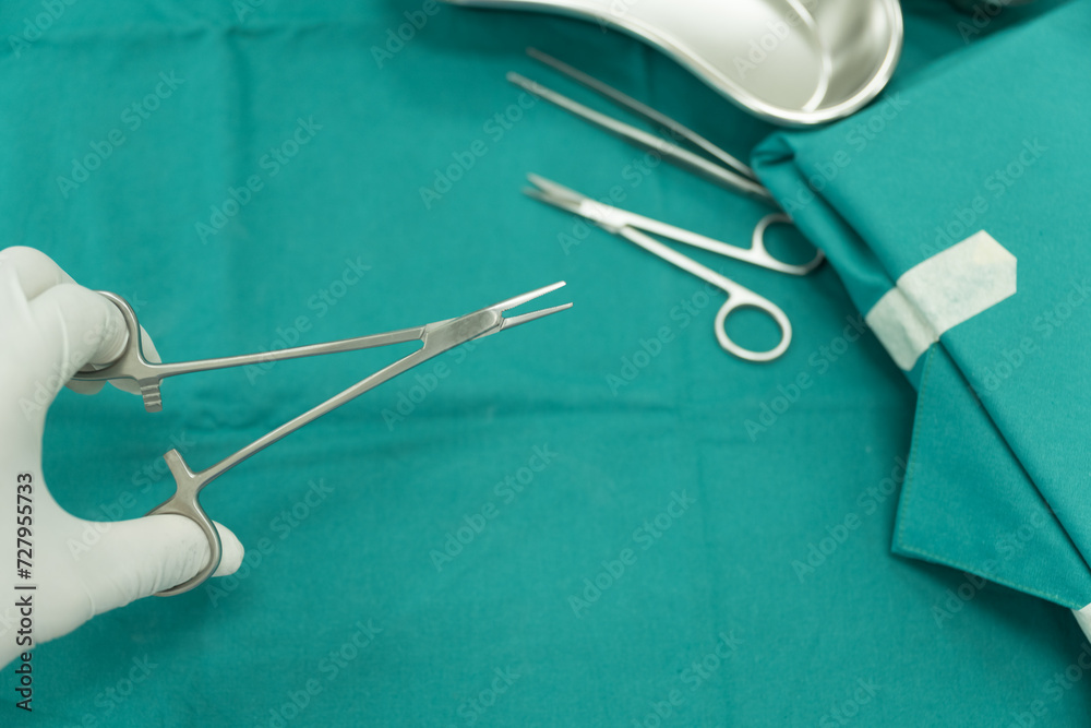 Surgeon doctor's hand with hygiene glove taking scissor surgical set and medical equipment on green surgical tray inside operating room.Sterile surgical instrument tool equipment for surgery. Surgeon doctor's hand with hygiene glove taking scissor surgical set and medical equipment on green surgical tray inside operating room.Sterile surgical instrument tool equipment for surgery.