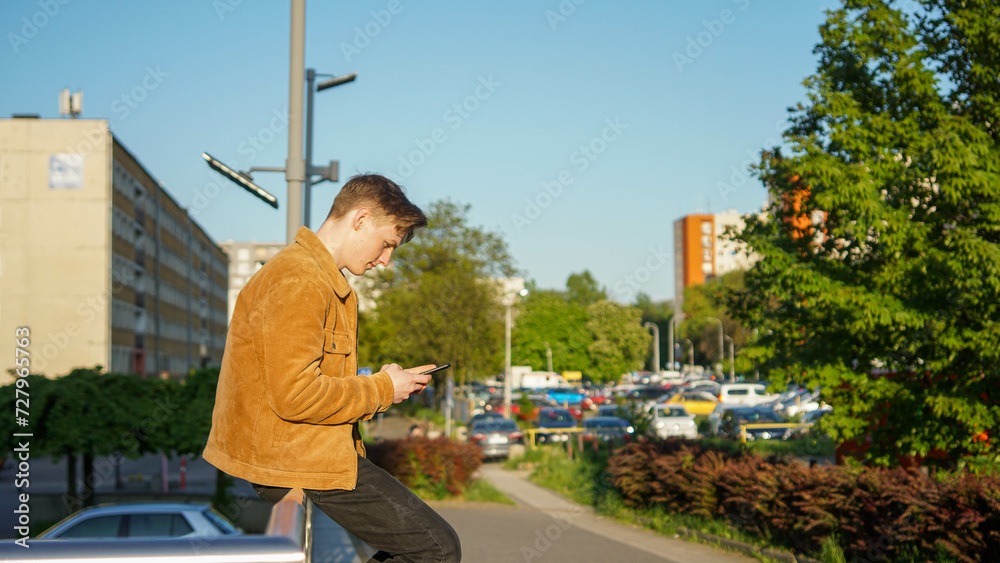 Teenager sitting with phone in sunshine in a city - Stock photo