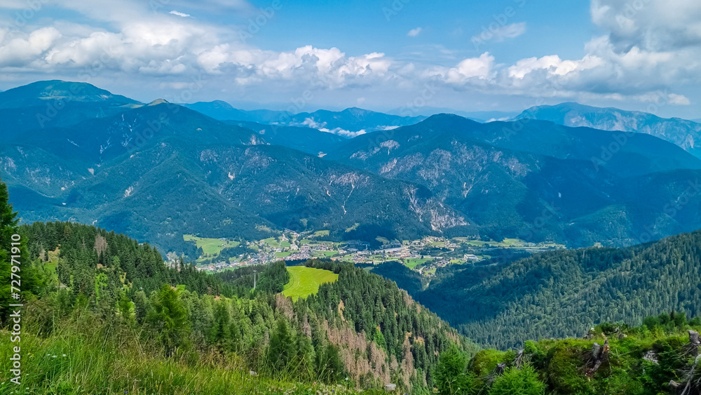 Fototapeta premium Aerial view of Tarvisio and Camporosso in valley Valcanale seen from observation point of Monte Lussari, Friuli Venezia Giulia, Italy. Looking at lush green alpine landscape of hills and meadows