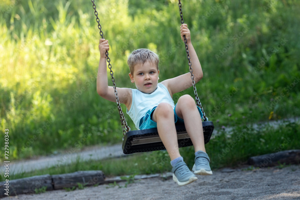 A little boy swings in time. sunny green grass background