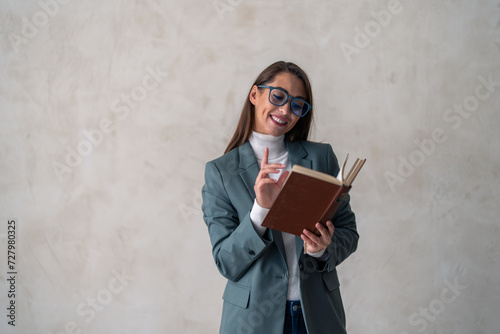 Young woman, model, university student, teacher with a book, wearing suit and eyeglasses, reading a book, standing confident in a studio for career vision, presentation, education, goals.