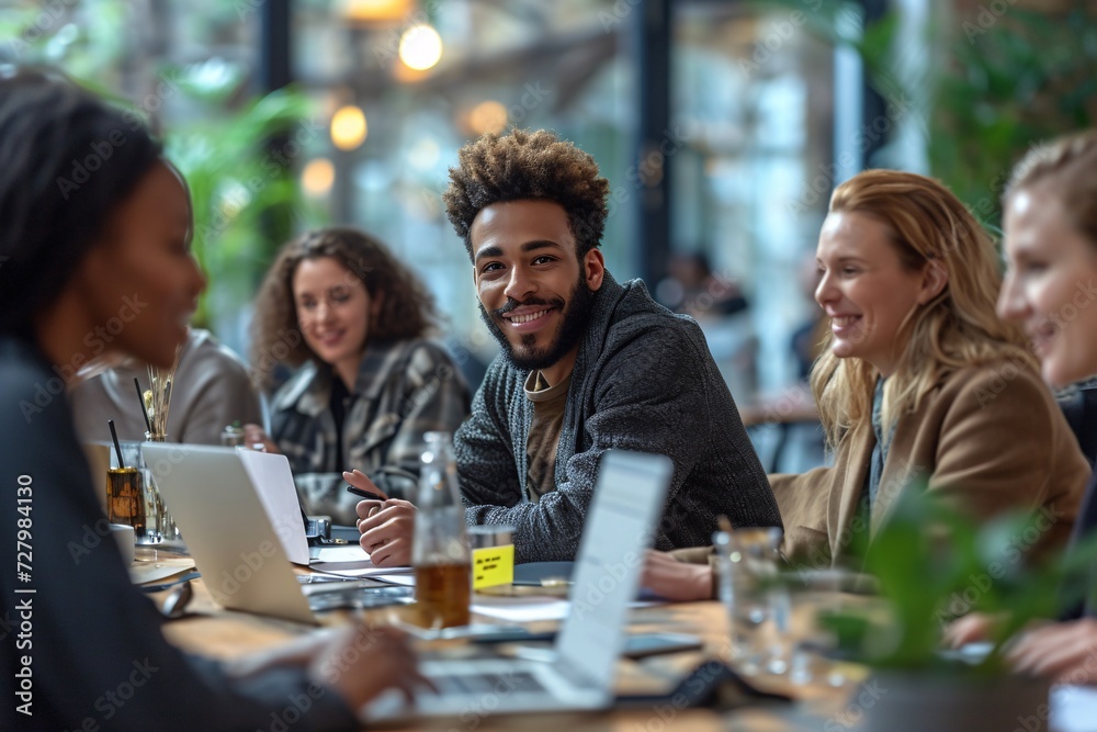 A diverse group of individuals, dressed in stylish clothing, sit around a table with their laptops and drinks, their faces filled with smiles as they engage in meaningful conversation indoors A diverse group of individuals, dressed in stylish clothing, sit around a table with their laptops and drinks, their faces filled with smiles as they engage in meaningful conversation indoors