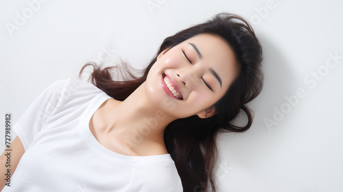 Close up picture of a smiling beautiful asian woman lying on a white background with eyes closed 
