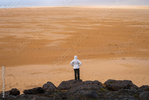 Girl standing on rock at Rauðasandur (Red Sand) beach in Westfjords, Iceland. Beautiful endless beach with sand that changes color depending on the weather and time of day photo