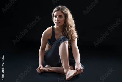Smiling young woman sitting on the floor with legs crossed, on a black backgroung