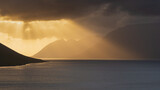 Dramatic sunset over fjord in Westfjords, Iceland. Rays of sunlight shining through dark clouds on water