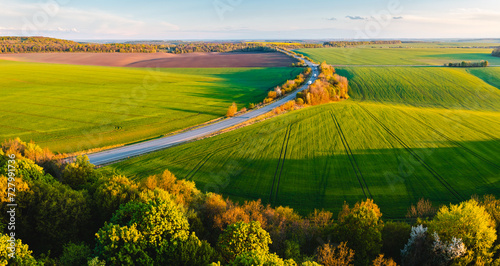From a bird's eye view, the road passes through farmland and green fields. photo