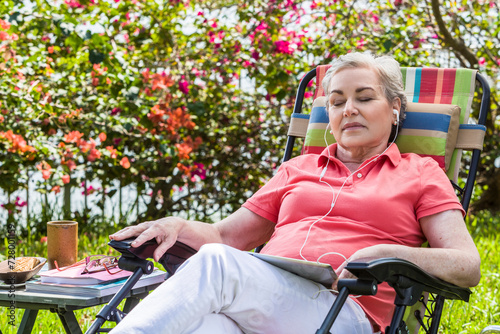 Mature woman sitting on chair in backyard sleeping whilke listening to tablet photo