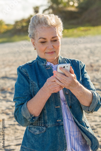 Mature woman at the beach using mobile phone. photo