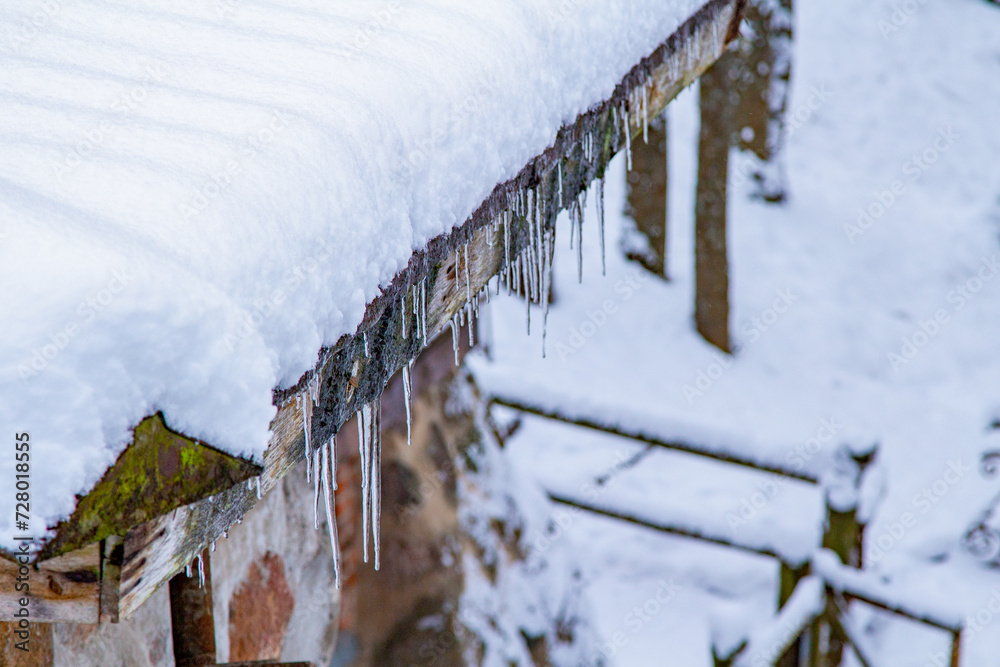 Fototapeta premium Icicles Hanging From A Roof. Roof Icicles. Spring Melting Snow. Snow Melt Roof. Moss Roof Winter. End of Winter.