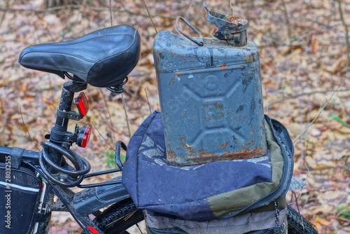 one iron rusty gray open dirty old canister stands on the trunk of a sports black mountain bike during the day on the street