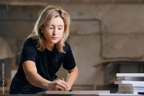 Happy worker young woman working in wooden furniture workshop, DIY marking dimensions of product