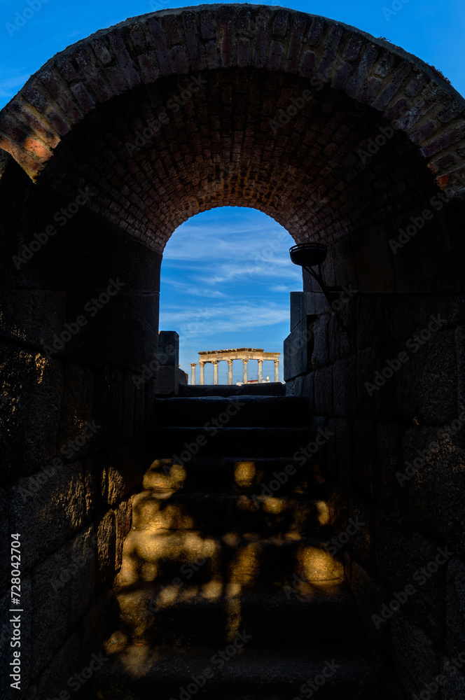 One of the arched entrances leading up stairs to the stands and the ancient stage of the Roman Theater of Mérida with a vaulted brick ceiling and granite stairs illuminated by dawn sunlight.