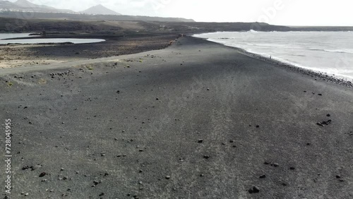 drone shot of a descent from above on black beach with clouds passing and ocean and mountains. 
lanzarote, spain.