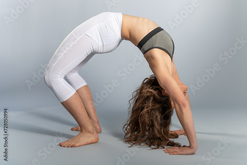 Young woman performing the wheel asana on a gray background