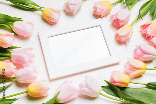 Fototapeta Naklejka Na Ścianę i Meble -  Light pink and yellow blooming tulips flowers row and white picture frame over white background. Spring holiday banner, happy easter card, mothers day concept. Flat lay, top view, copy space