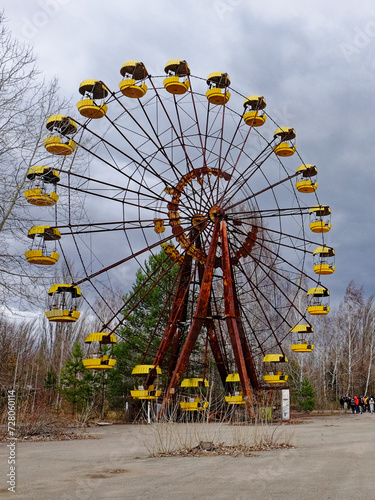 A deserted Ferris wheel surrounded by bare trees under a cloudy sky.