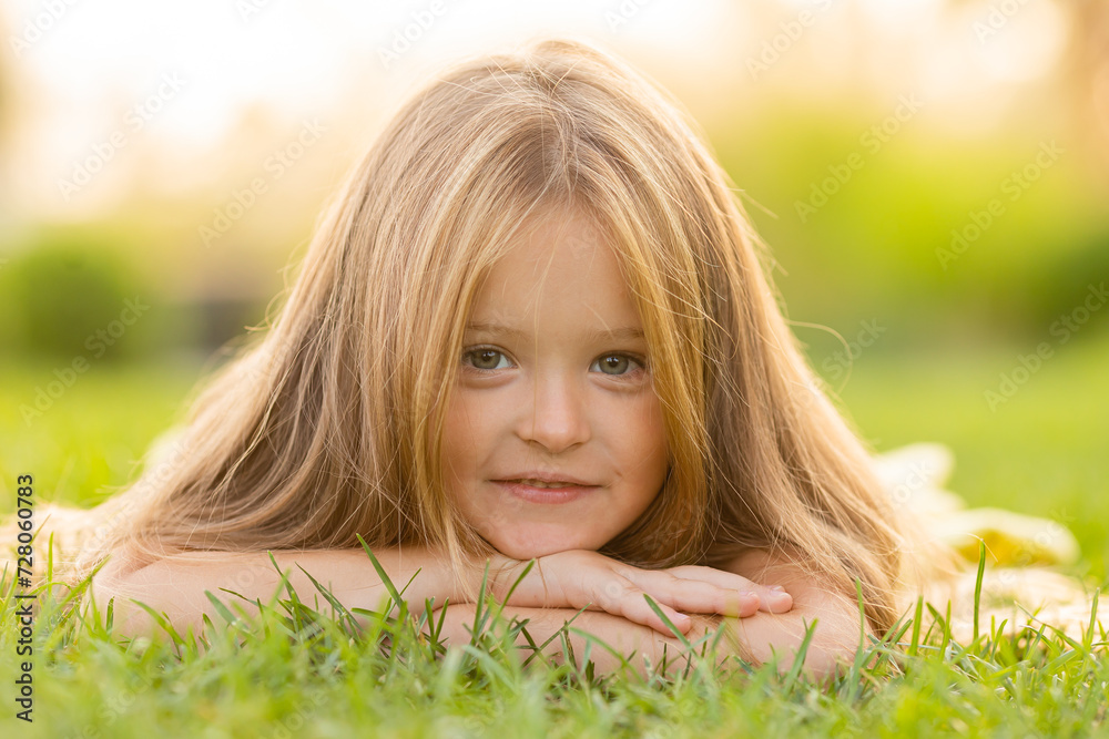beautiful little girl with long blonde hair lies on a green lawn in the summer in a city park beautiful little girl with long blonde hair lies on a green lawn in the summer in a city park