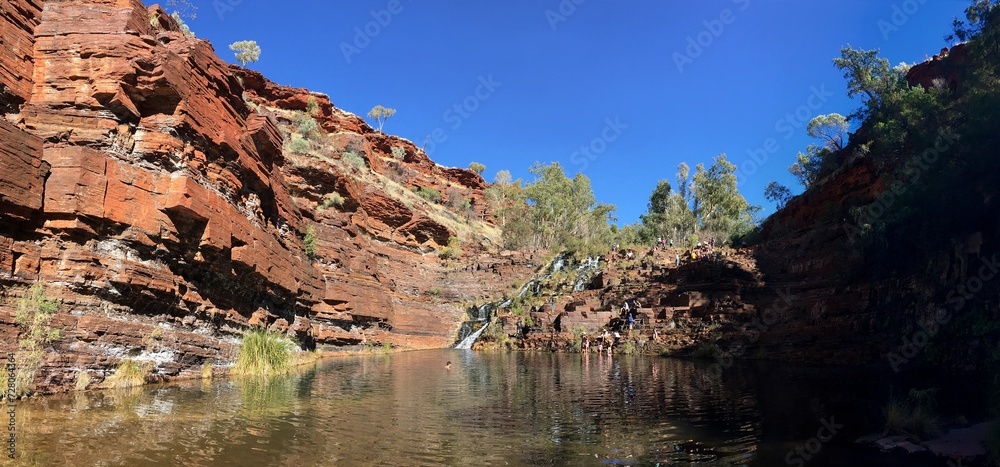 Rocks of the Fortescue Falls in Karijini, WA, water pool with unrecognizable people