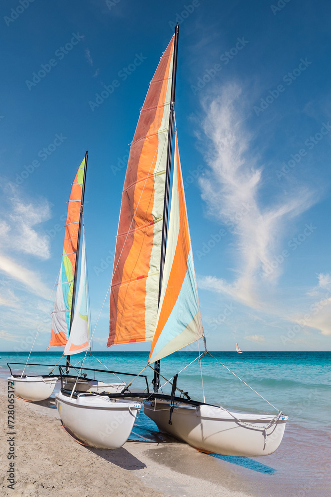 Naklejka premium Colorful sailing catamaran on the beach of the Varadero - Cuba. Turquoise blue Atlantic water and blue sky with white clouds.