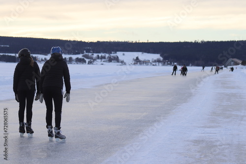 People in the center of the city are skating and walking on an icy lake. 