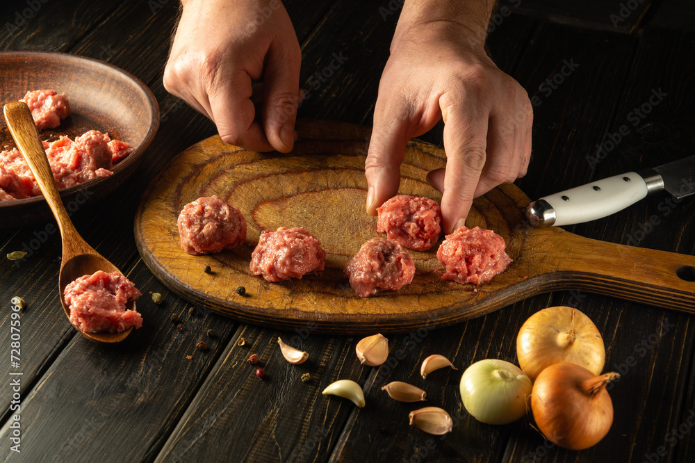 A man hand puts a meatball on a kitchen board. Cooking meat on the kitchen table. Cooking, recipes and nutrition concept