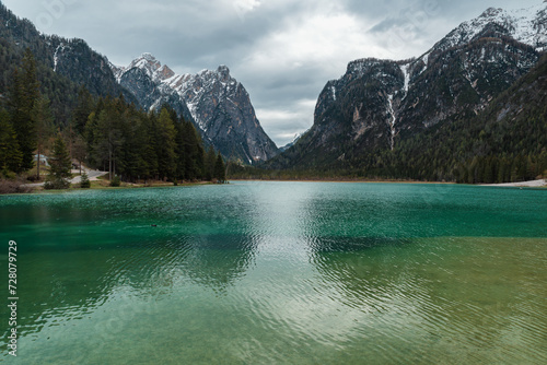 Moody landscape with turquoise water alpine lake Lago di Dobbiaco in Dolomites mountains  Cortina dAmpezzo  Italy on cloudy spring day. Lake Toblacher See in the forest in Dolomiti
