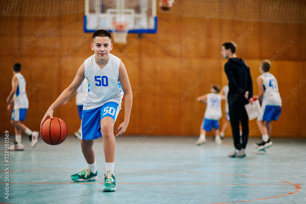 A young basketball kid is dribbling a ball on court on training. A young basketball kid is dribbling a ball on court on training.