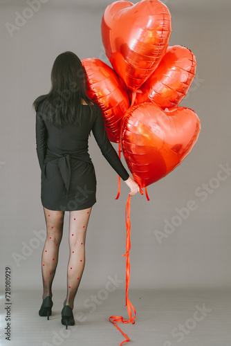 Elegant woman in black short dress with red balloons heart shape. Celebration of St Valentine's day. 14 February concept