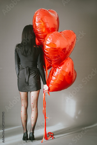 Elegant woman in black dress with red balloons heart shape. Celebration of St Valentine's day