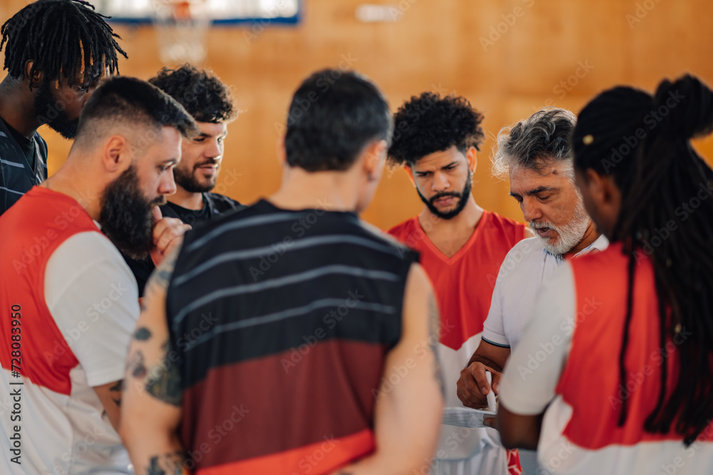 Fototapeta premium A senior coach is working on game tactic with interracial basketball team.