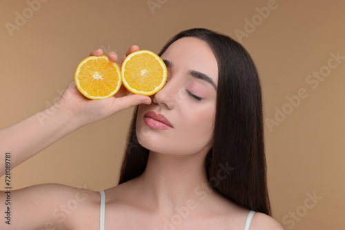 Beautiful young woman with pieces of orange on beige background