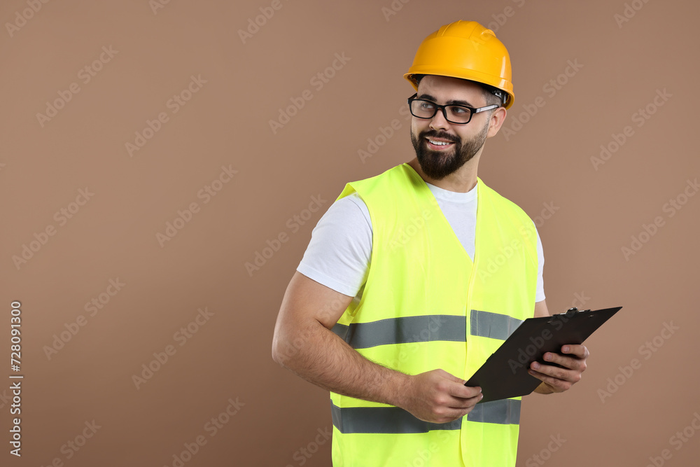 Engineer in hard hat holding clipboard on brown background, space for text Engineer in hard hat holding clipboard on brown background, space for text